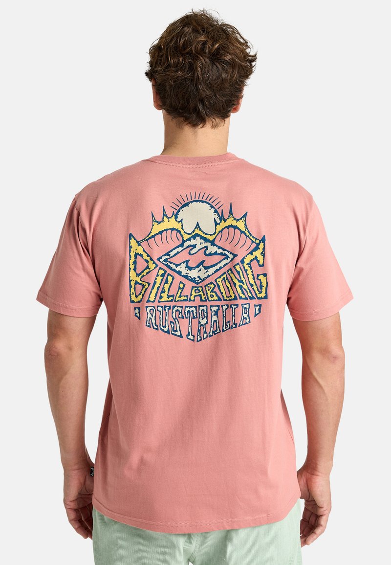 T-shirt en coton rose avec un design graphique au dos comportant des éléments bleus et jaunes, incluant des vagues et le texte "BILLABONG AUSTRALIA."