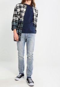 Koszula w kratę w kolorze czarnym, białym i niebieskim na granatowej koszulce. Jasnoniebieskie dżinsy i czarne trampki dopełniają strój. Casulowy design i krój.