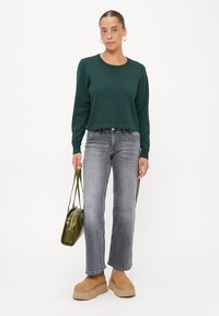 Grønn cropped genser, grå jeans, lysebrune plattform støvler, og en liten olivenfarget veske. Modellen står mot en hvit bakgrunn.
