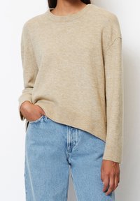 Pull en laine beige avec encolure ronde, poignets et ourlet côtelés. Associé à un jean taille haute bleu clair. Texture douce, coupe décontractée.