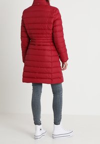 Röd puffjacka med horisontella quiltade rutor, hög krage och figursydd midja. Kombinerad med grå jeans och vita högsneakers.