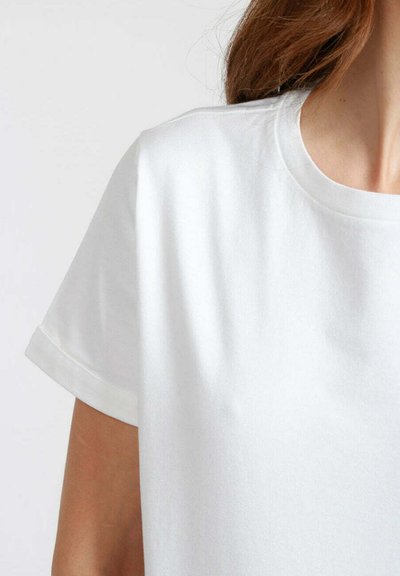 T-shirt bianco in cotone con scollo rotondo e maniche corte, caratterizzato da una texture liscia e orli delle maniche arrotolati. Nessun motivo o grafica visibile.