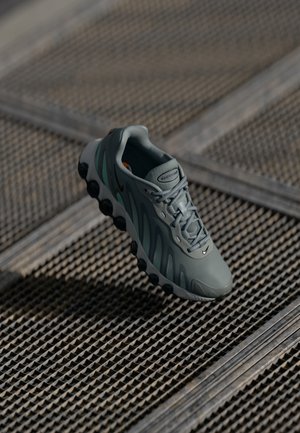 Baskets Nike Air Max grises avec des détails noirs sur la semelle, reposant sur une surface de grille métallique texturée sous une lumière douce.