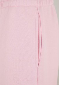 Lyserøde sweatpants lavet af blødt stof med elastisk talje, sidelommer og broderet logo-detalje nær kanten.