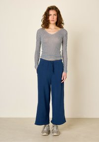 Haut à manches longues rayé en bleu marine et blanc, associé à un pantalon large bleu marine. Le haut présente un col en V ; le pantalon a une taille élastique.