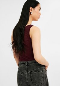 Maroon tank top valmistettu sileästä materiaalista, yhdistettynä korkeavyötäröisiin, tummanharmaisiin farkkuihin, joissa on haalistuneet yksityiskohdat ja takataskut.