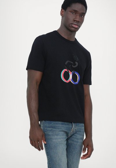 T-shirt noir avec un design graphique coloré, comprenant des cercles et du texte. Manches courtes, col rond, en mélange de coton, texture lisse.
