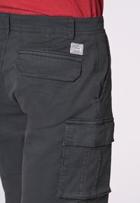 Pantaloni cargo neri con numerosi taschini laterali, un design elegante e un tessuto testurizzato. Un'etichetta sulla tasca posteriore riporta la scritta "USPA."