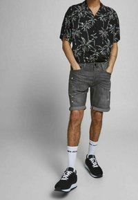 Short-sleeve black floral shirt, gray denim shorts with rolled cuffs, black sneakers, and white socks with branding. Textured materials and patterns.
