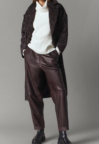 Brune læderbukser, hvid kabelstrikket sweater og en mørk tekstureret frakke. Sorte ankelstøvler fuldender outfittet.