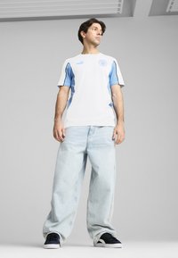 Bílý a světle modrý sportovní dres s krátkými rukávy, s logem. V kombinaci s oversized světle modrými džínami a černými teniskami.