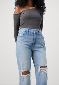 Šedý pruhovaný top bez ramínek spárovaný s světle modrými džíny s vysokým pasem, které mají vytrhané kolena a uvolněný střih.