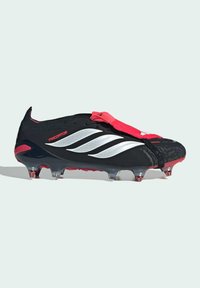Μαύρο και κόκκινο ποδοσφαιρικό παπούτσι Adidas Predator με λευκές ρίγες, εφοδιασμένο με καρφιά στη σόλα και κόκκινο κάλυμμα κορδονιών σε ανοιχτό φόντο.
