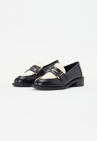 Sorte skinnloafers med hvit skinnakent og gullhardware. Rund tå, lav blokkhelt, strukturert overflate, klassisk design.