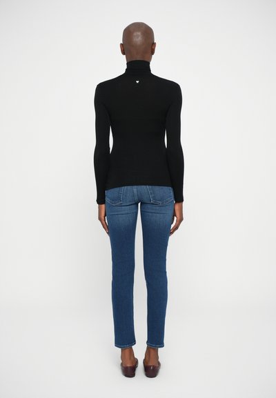 Maglione a collo alto nero con maniche lunghe, vestibilità slim; abbinato a jeans blu, gamba dritta, leggermente elasticizzati e orlo alla caviglia.