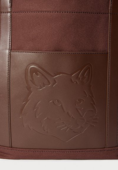 Barna táska texturált felülettel, domború rókafej díszítéssel. Az anyag sima bőrhatású és szövet elemek keveréke.
