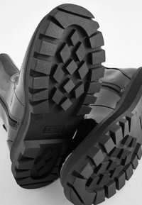 Schwarze Lederstiefeletten mit strukturierten Gummisohlen, die tiefen Profil und Zickzackmuster aufweisen, einschließlich seitlicher Reißverschlüsse für ein einfaches Anziehen.