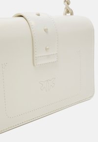 Borsa in pelle bianca con chiusura a patta, caratterizzata da borchie decorative, logo impresso e dettagli di cucitura sottili. Textura liscia.