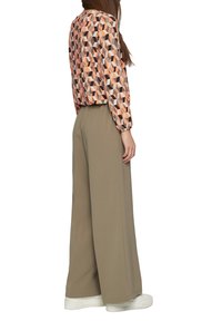 Lange, wijde beige broeken in combinatie met een losjes passend blouse met een herhaald geometrisch patroon in perzik-, bruin- en grijstinten.
