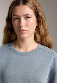 Ljusblå långärmad sweatshirt med rund hals, texturerad tyg och subtila sömmar vid axlarna.