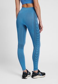 Blå atletiska leggings med en texturerad design, med ett mönstrat rand längs den yttre benet. Högmidjad passform och mjukt material.