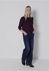 Mörklila långärmad topp i kombination med blå vida jeans. Klädseln har en avslappnad passform med framfickor och en mjuk textur.