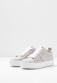 Baskets grises en cuir de crocodile avec des lacets plats blancs et une épaisse semelle blanche. Texture lisse avec une finition légèrement brillante.