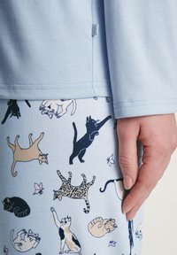 Lichtblauwe top met een gladde textuur, gecombineerd met gestreepte pyjama-broek die verschillende kattenillustraties en kleine vlinders bevat.