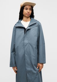 Ανοιχτό μπλε αδιάβροχο μπουφάν με φερμουάρ, ψηλό γιακά και πλαϊνές τσέπες, με άνετη εφαρμογή και λεία υφή.