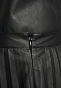 Robe en cuir noir avec une finition texturée, une fermeture éclair centrée et des détails plissés sur la partie inférieure.
