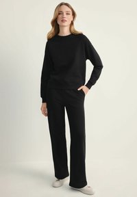 Czarna bluza z okrągłym dekoltem i rękawami raglanowymi, zestawiona z czarnymi spodniami dresowymi o luźnym kroju i lekko rozszerzających się nogawkach.