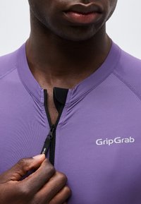 Κλείσιμο εικόνας ενός ατόμου που τραβά το φερμουάρ ενός μοβ ποδηλατικού τζέρσεϊ GripGrab με μαύρο έλκτη φερμουάρ.