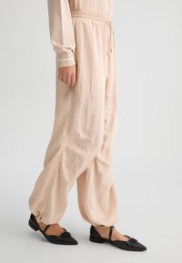 Pantaloni leggeri, rosa pallido, con vita elastica e cordoncino, caratterizzati da una silhouette rilassata e da un tessuto testurizzato. Ballerine nere con dettaglio a fibbia.