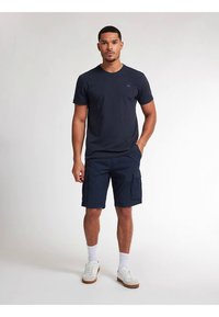 Pánské tmavě modré bavlněné tričko s kulatým výstřihem; doplněné o tmavě modré cargo kraťasy s bočními kapsami a rovný střihem; bílé tenisky.