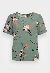 Top verde de mangas curtas com um padrão floral em rosa, branco e preto, com um decote redondo e um detalhe em forma de chave na parte de trás.