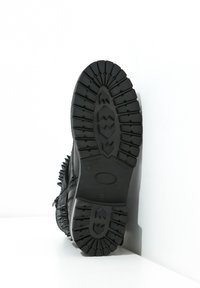 Svart boot med en texturerad gummisula, som har spikdetaljer längs sidan, robust design och en lågt profilerad siluett.