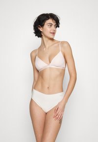 Bralette triangulaire rose clair avec des fines bretelles et un détail torsadé à l'avant, associée à une culotte haute sans coutures blanche. Tissu lisse.
