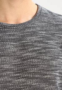 Närbild av en svartvit texturerad stickad crewneck-tröja som bärs på en persons övre bröst och hals.