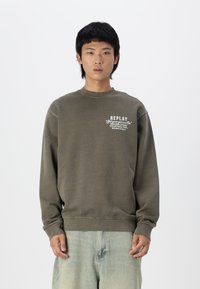 Sudadera verde oliva con cuello redondo, mangas largas y puños acanalados. Presenta el texto del logo "REPLAY" en blanco en la parte izquierda del pecho.