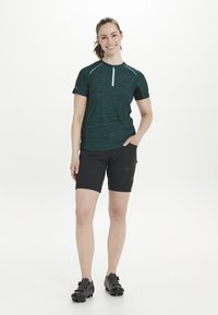 Teal och svart kortärmad skjorta med zipkrage, kombinerad med svarta shorts. Har ett texturerat tyg och sidoficka med dragkedja på shortsen.