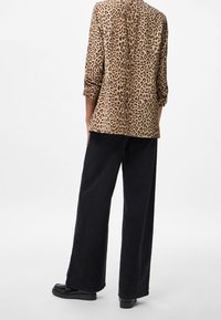 Marynarka w brązowo-czarny wzór w panterkę, z rękawami do łokcia, zestawiona z czarnymi spodniami o szerokich nogawkach i czarnymi butami na platformie.