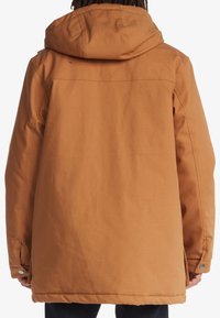 Hnědá bunda s kapucí s volným střihem, vyrobená z texturované látky. Má zapínání na patentky a čistý, bezšvový design zad.