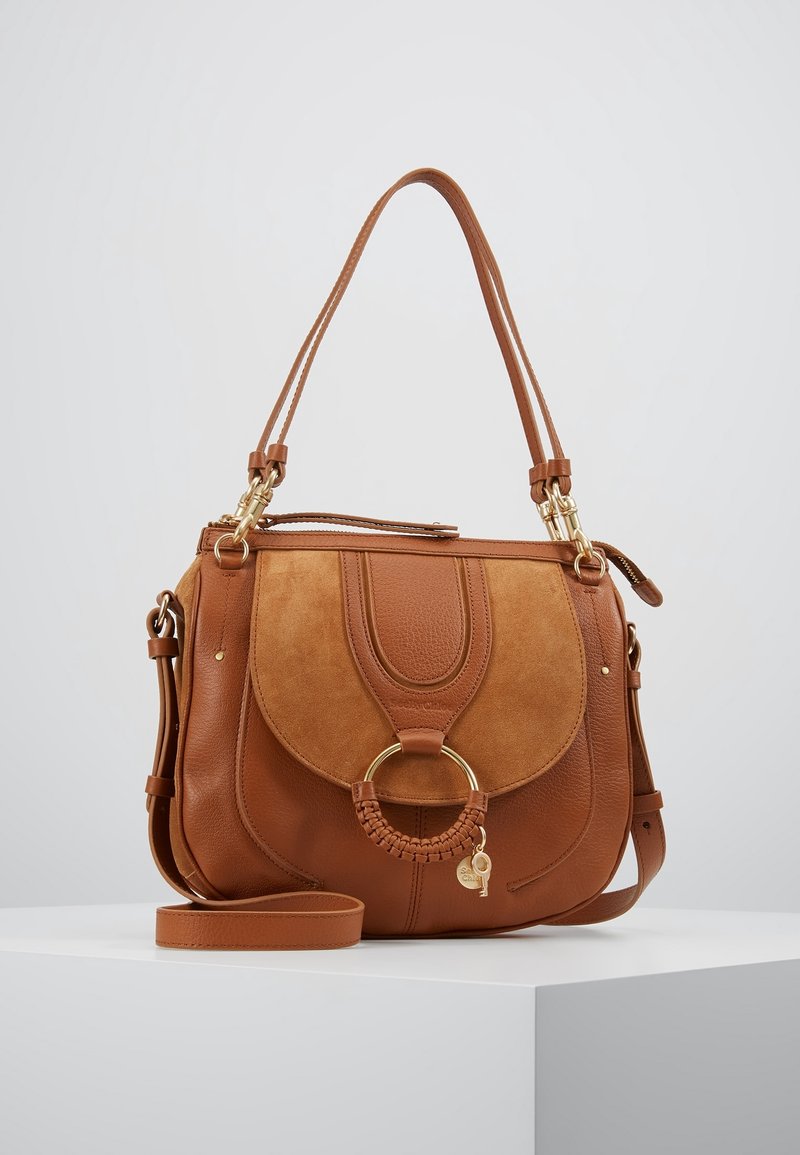 Brun læder skuldertaske med ruskind detaljer, oval form, flettet udsmykning på en guldring og justerbare stropper.