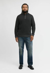 Dark gray, textured knit pullover with a high collar and three-button placket, paired with light blue straight-leg jeans and black shoes.