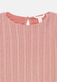 Ροζ γυαλιστερό φόρεμα με κατακόρυφες πτυχώσεις, στρογγυλή λαιμόκοψη, κλείσιμο με κουμπί σε σχήμα κλειδαριάς και εμφανή ετικέτα Guess μέσα στη γιακά.