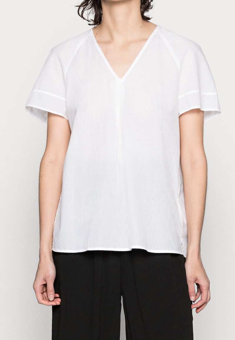 Witte, korte mouwen V-hals blouse met subtiele verticale strepen en een relaxte pasvorm. Gemaakt van lichte stof met zijsplitten voor extra comfort.