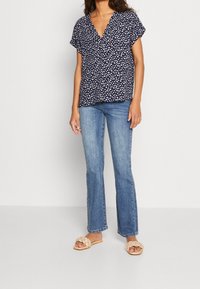Blusa de manga corta navy con estampado floral blanco y diseño de escote en V, combinada con jeans acampanados de color azul claro y sandalias de trenzado en color beig.