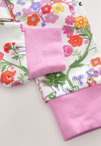 Tissu imprimé floral blanc avec des fleurs colorées, comportant des poignets côtelés roses. Le motif inclut un petit lapin et des feuilles. Texture douce en coton.