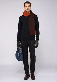 Černý svetr, hnědý šátek s třásněmi, černé kalhoty, kožené rukavice, hnědé boty a modrá taška se stříbrným zipem.