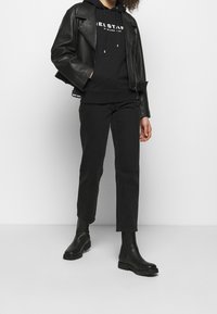 Svart läderbikerjacka, svart hoodie med vit logotyp, svarta slim-fit-byxor och svarta ankelstövlar med texturerad sula.